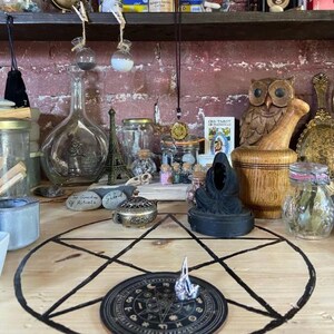 Puede incluir: Una colecci&oacute;n de objetos espirituales y ocultos, que incluye frascos de vidrio, un b&uacute;ho de madera, una estatua negra y un dise&ntilde;o de pentagrama sobre una superficie de madera. Tambi&eacute;n son visibles varias botellas peque&ntilde;as y una peque&ntilde;a Torre Eiffel.