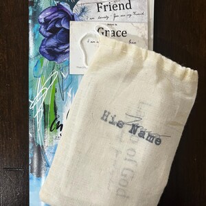 May include: An assortment of faith-based items, including a booklet with a blue floral design and the words "in Christ", a card with "Jesus is my Friend", and a small drawstring bag with "His Name" printed on it.