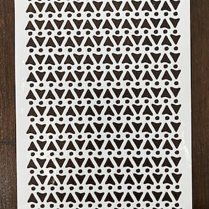 May include: A white stencil with a repeating pattern of stylized arrows and dots. The design is cut out, creating negative space. The bottom of the stencil includes the text "©2016 Joggles.com #33836".