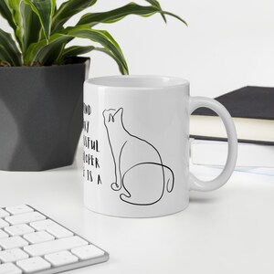 May include: White ceramic mug with a black line drawing of a cat sitting on its haunches. The text on the mug reads "A kind, quirky, successful developer is a cat person."