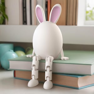 May include: A white ceramic bunny rabbit figurine with pink ears sitting on a stack of books. The bunny has articulated legs and is sitting with its legs crossed.