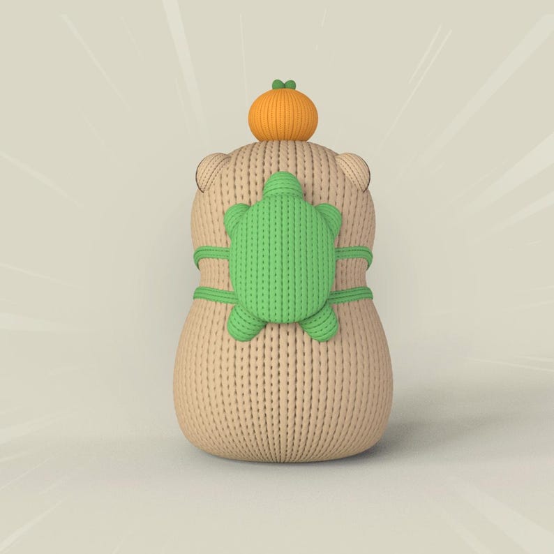May include: A beige knitted plush toy with a green turtle on its back and an orange pumpkin on its head.