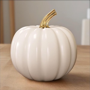 Peut inclure: Une citrouille en céramique blanche avec une finition brillante et une tige dorée. La citrouille présente des rainures verticales et est un objet décoratif, idéal pour la décoration d'automne.