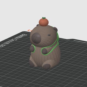 May include: A brown and green 3D printed capybara figurine wearing a green scarf and holding an orange pumpkin on its head.