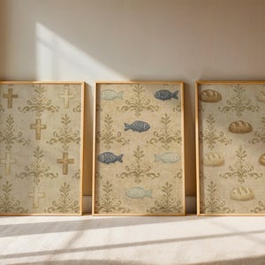 May include: Three framed art prints with gold frames. The prints feature repeating patterns of crosses, fish, and bread on a beige background with a floral design. The art has a vintage, rustic aesthetic.