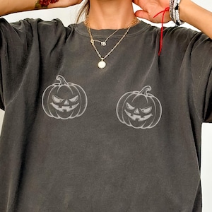 May include: A charcoal gray crewneck t-shirt featuring two white line-art illustrations of jack-o'-lanterns with jagged, smiling faces printed on the front. The shirt has a relaxed fit and a faded, vintage-style wash throughout the fabric.