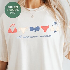 Peut inclure: T-shirt cr&egrave;me avec une rang&eacute;e de bikinis illustr&eacute;s rouges, blancs et bleus. L'inscription "all american summer" est imprim&eacute;e en bleu en dessous. Un cercle vert avec du texte est visible en haut &agrave; gauche.