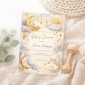 May include: A baby shower invitation with a celestial theme. The design features a sleeping baby on a crescent moon, stars, clouds, and the text "Baby Shower" and "Olivia Anderson". A wooden rattle is next to the invitation.