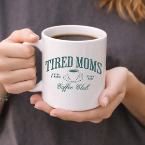 May include: A white ceramic mug with a black handle and the text "But First, Coffee" in a handwritten style. The mug is on a white surface. The mug is 4 inches tall.