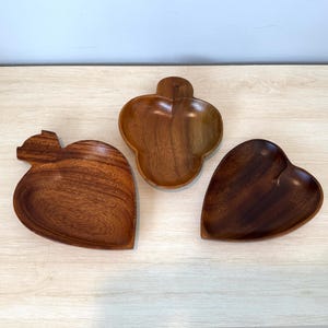 May include: Three wooden heart-shaped serving dishes. The dishes are made of dark brown wood and have a smooth, polished finish.