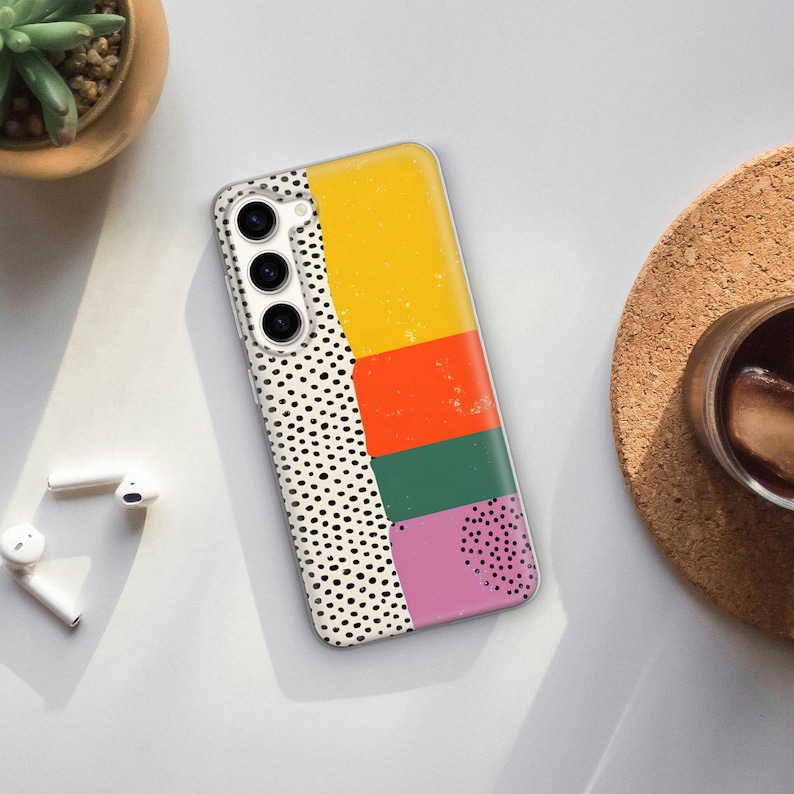 May include: A white phone case with a geometric design featuring black polka dots, yellow, orange, green, and pink squares.