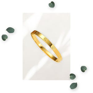 May include: A gold bangle bracelet with a simple design featuring small circles around the band.