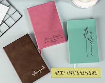 Könnte beinhalten: Drei personalisierte Notizbücher mit unterschiedlichen Designs. Das erste Notizbuch ist braun mit dem Namen "Abigail" in goldenen Buchstaben. Das zweite Notizbuch ist rosa mit dem Namen "Henry Cooper" und dem Titel "Manager" in schwarzen Buchstaben. Das dritte Notizbuch ist hellgrün mit einem floralen Design und dem Namen "celine" in schwarzen Buchstaben.