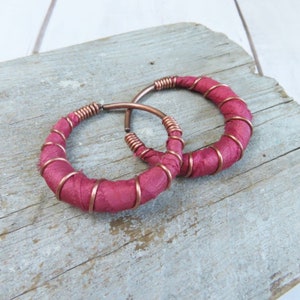 May include: A pair of large hoop earrings made with copper wire wrapped with a deep burgundy fabric.