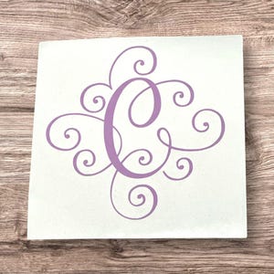 May include: A white square tile with a purple letter C surrounded by decorative swirls.