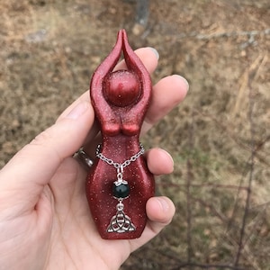 May include: Red glitter goddess statue with a silver chain and a green stone pendant. The pendant has a silver Celtic knot design.