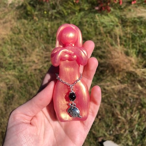 May include: A pink and gold resin figurine of a woman with a silver chain and charm necklace. The charm is a silver pomegranate.