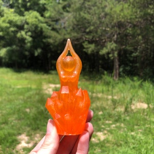 May include: Orange resin sculpture of a woman in a yoga pose, sitting on a crystal base.