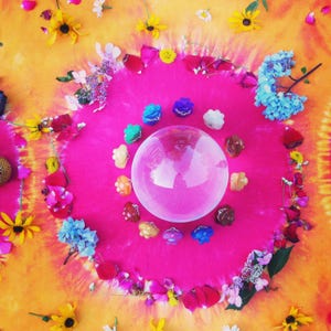 May include: A crystal ball surrounded by colorful crystals on a pink and orange tie-dye background with flowers and petals.