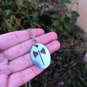 May include: A silver necklace with a pendant shaped like an oval. The pendant has a cutout design of a double-headed axe.