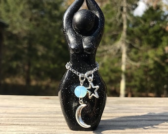 May include: Black goddess statue with a silver chain necklace with a crescent moon, star, and opal bead charms.