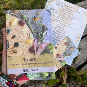 May include: A book titled "Return: The Sacred Art of Coming Home to Yourself" by Molly Remer. The cover features a collage of crystals, flowers, and a wooden board. A card with text is also visible.
