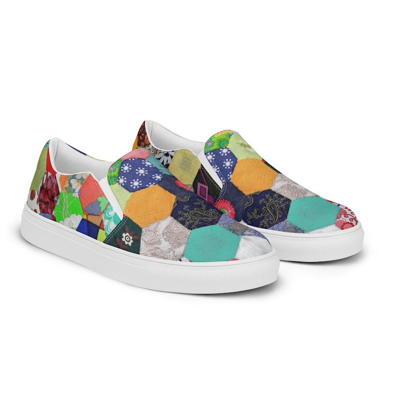 May include: A pair of white canvas slip-on shoes with a colorful patchwork design. The design features a variety of fabrics in different colors and patterns, including floral, paisley, and geometric prints.
