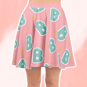 May include: A pink skater skirt with a repeating pattern of teal letter "B" shapes outlined in white. Small yellow triangles are scattered across the fabric. The skirt is knee-length and has a fitted waistband.