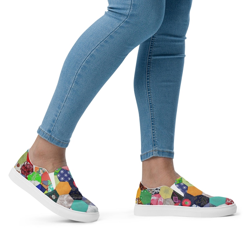 May include: A pair of white canvas slip-on shoes with a colorful patchwork design. The shoes feature a variety of geometric shapes and patterns in shades of red, green, blue, yellow, and orange.
