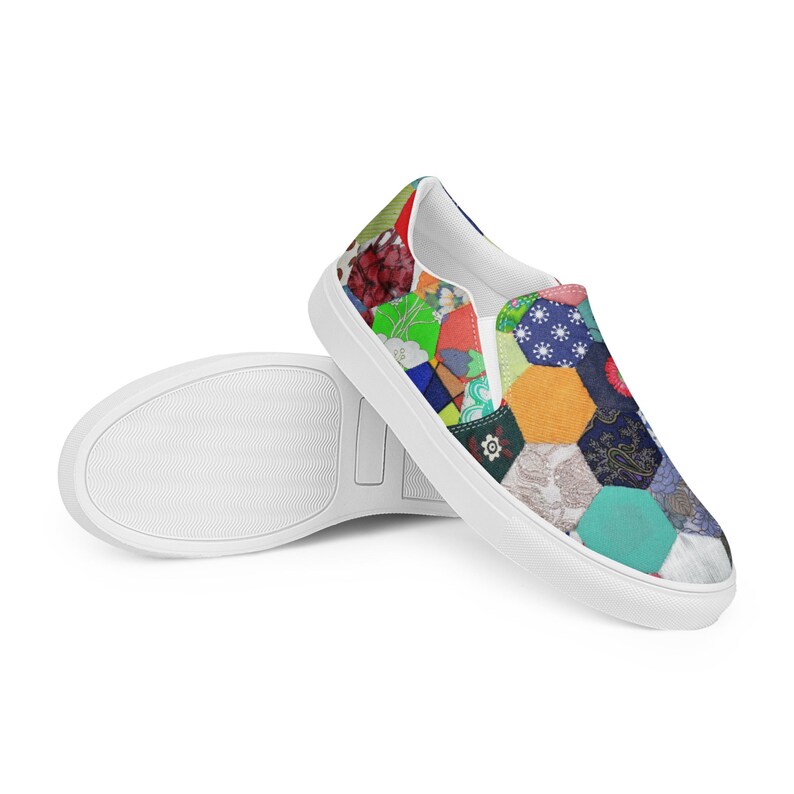 May include: White slip-on canvas shoes with a colorful patchwork design. The design features a variety of geometric shapes and patterns in shades of blue, green, red, yellow, and orange.