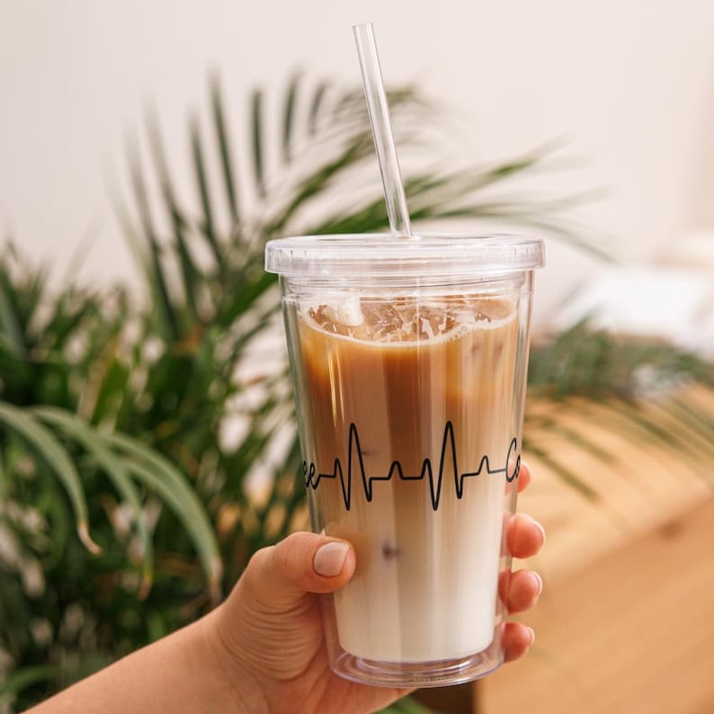 May include: A clear plastic tumbler with a black lid and a black straw. The tumbler is filled with iced coffee and has a black heartbeat graphic on the side. The text "Coffee" is partially visible on the tumbler.