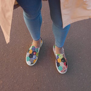 May include: A pair of slip-on shoes with a colorful patchwork design. The shoes are made of canvas and have a white sole.