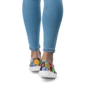 May include: A pair of white canvas slip-on shoes with a colorful patchwork design. The shoes have a rounded toe and a white rubber sole.