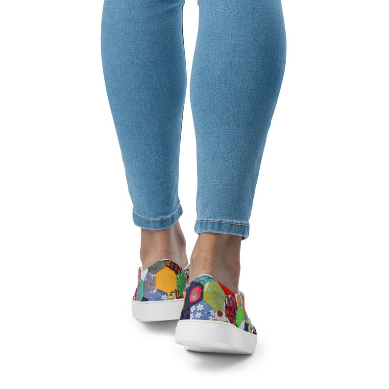 May include: A pair of white canvas slip-on shoes with a colorful patchwork design. The shoes have a rounded toe and a white rubber sole.