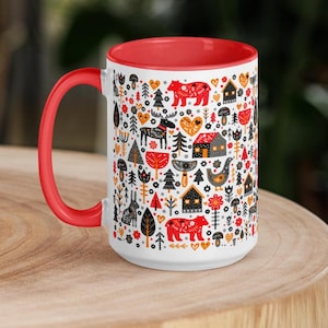 May include: A white ceramic mug with a red rim and handle. The mug features a colorful Scandinavian-inspired pattern with animals, houses, and trees. The pattern includes red, orange, yellow, black, and gray colors.