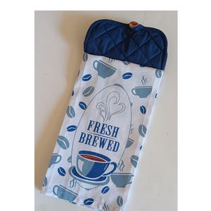May include: A white kitchen towel with a blue and gray coffee cup design. The towel has the text "FRESH BREWED" and a blue pot holder with a button.