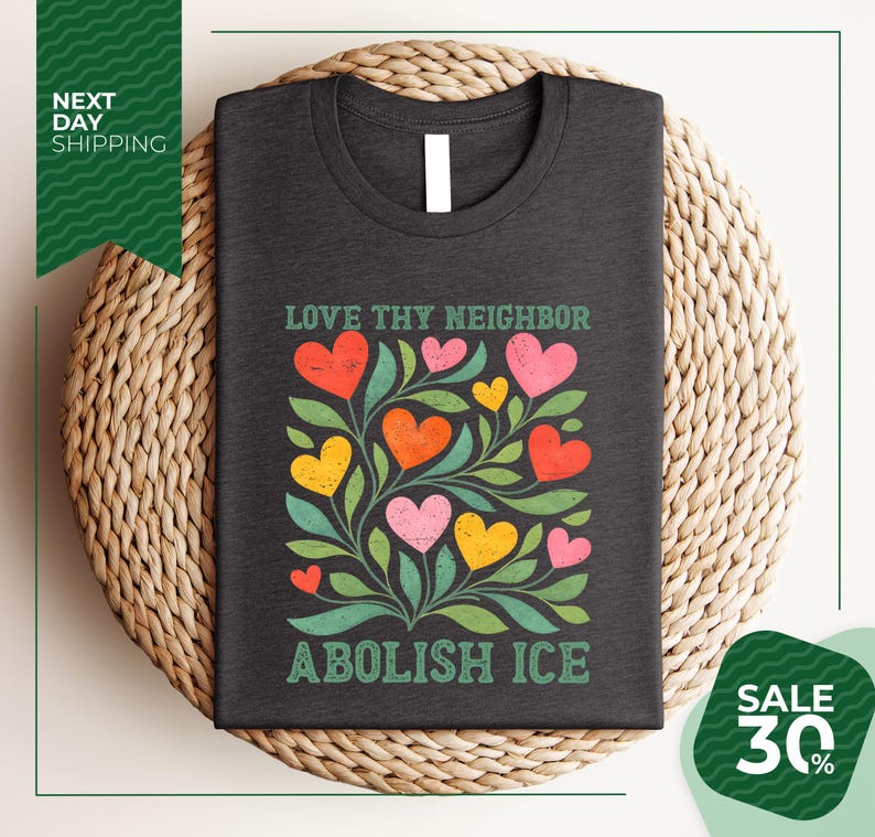 a black t-shirt with a colorful graphic design of hearts and leaves, along with the text "Love thy neighbor, Abolish ice" printed on it. The t-shirt is displayed on a woven basket, and there is a green banner with text that reads "Next day shipping" and "SALE 30%".