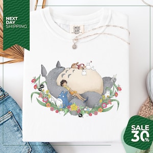 a white t-shirt with a colorful illustration of a cat surrounded by various animals and flowers, including a blue bird. The t-shirt is displayed on a white background, and there is a sale sign indicating a 30% discount.