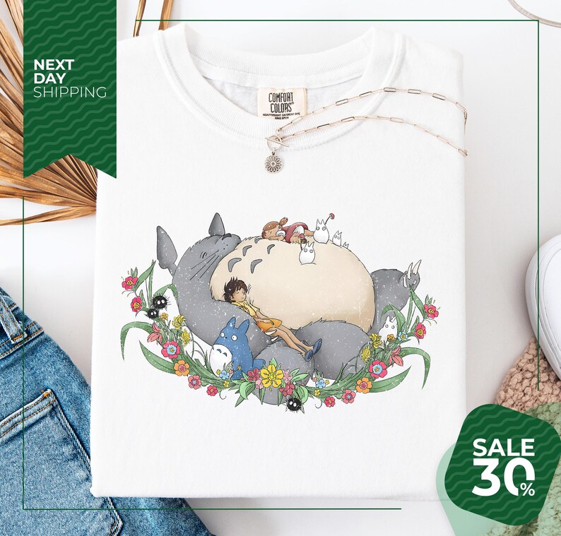 a white t-shirt with a colorful illustration of a cat surrounded by various animals and flowers, including a blue bird. The t-shirt is displayed on a white background, and there is a sale sign indicating a 30% discount.