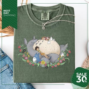 a green t-shirt with a colorful illustration of a cat surrounded by various animals and flowers. The t-shirt is displayed on a white background, and there is a sale sign indicating a 30% discount.
