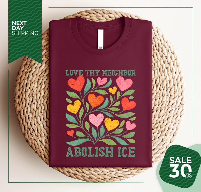 a burgundy t-shirt with a colorful graphic design of hearts and leaves, along with the text "Love thy neighbor" and "Abolish ice" printed on it. The t-shirt is displayed on a woven basket, and there is a green banner with white text that reads "Next day shipping" and "SALE 30%".