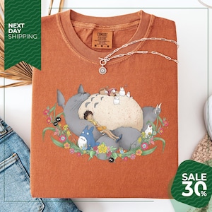 a red t-shirt with a colorful graphic design depicting a cat surrounded by various animals and flowers. The t-shirt is displayed on a white background, and there is a sale sign indicating a 30% discount.