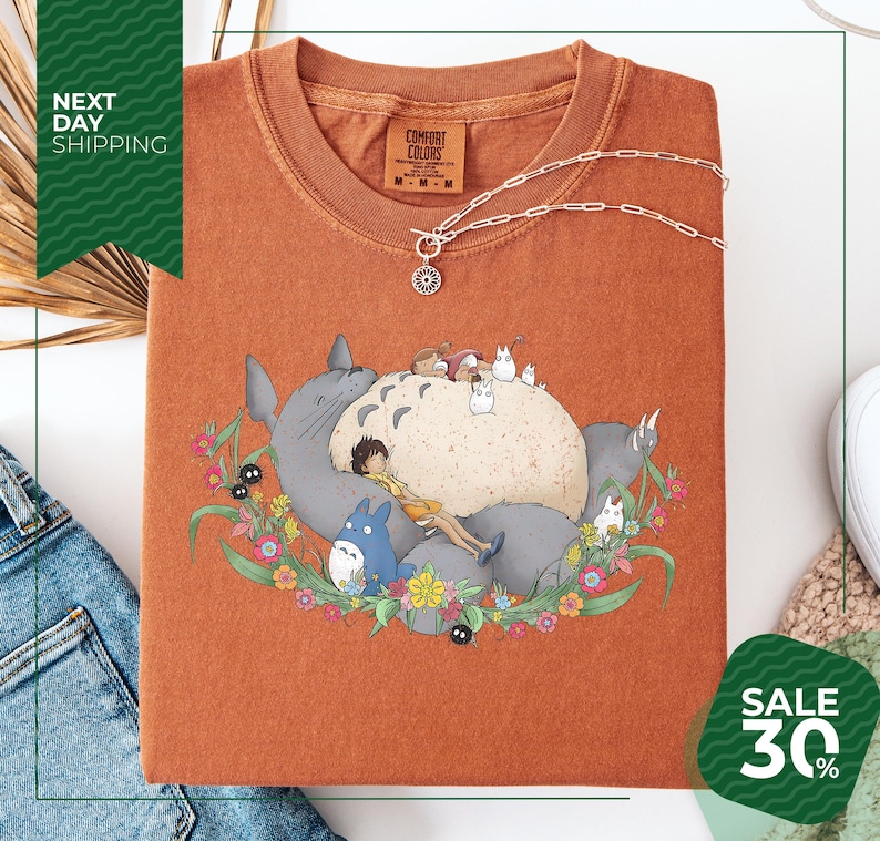 a red t-shirt with a colorful graphic design depicting a cat surrounded by various animals and flowers. The t-shirt is displayed on a white background, and there is a sale sign indicating a 30% discount.