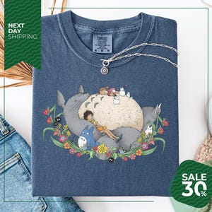 a blue t-shirt with a colorful illustration of a cat surrounded by various animals and flowers, including a bird and a dog. The t-shirt is displayed on a white background, and there is a sale sign indicating a 30% discount.