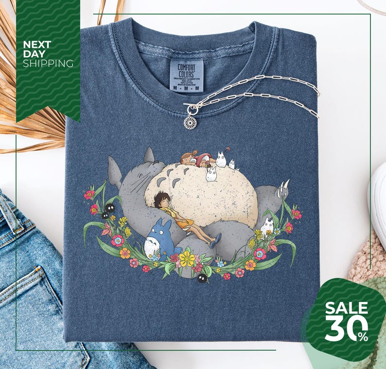 a blue t-shirt with a colorful illustration of a cat surrounded by various animals and flowers, including a bird and a dog. The t-shirt is displayed on a white background, and there is a sale sign indicating a 30% discount.