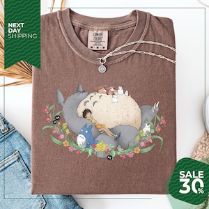 a brown t-shirt with a colorful graphic design depicting a cat surrounded by various animals and flowers. The t-shirt is displayed on a white background, and there is a sale sign indicating a 30% discount.