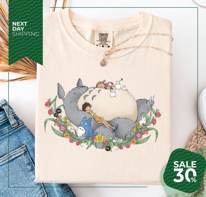 a white t-shirt with a colorful graphic design depicting a cat surrounded by various animals and flowers. The t-shirt is displayed on a white background, and there is a sale sign indicating a 30% discount.