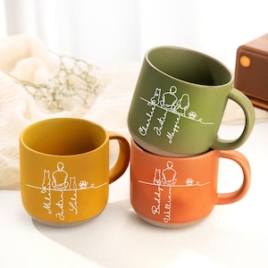 May include: Four ceramic mugs in shades of yellow, green, and orange are stacked. Each mug features a white line drawing of a person, pets, and names. The mugs have a matte finish and a light-colored base. The mugs are for beverages.