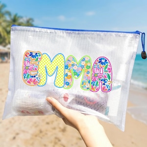 May include: A clear, zippered pouch with a blue zipper and pull. The word "EMMA" is printed on the front in colorful floral and checkered patterns. The pouch is held up on a beach with the ocean in the background.