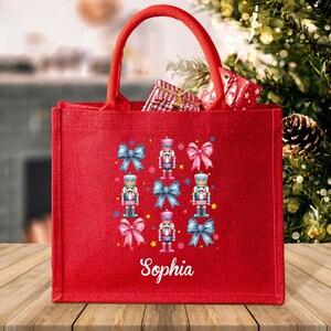 May include: Red jute tote bag with a Christmas nutcracker design and the name "Sophia" printed on the front.